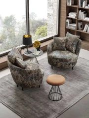 Privè — Elegant armchair with cushions resting on a slim, asymmetrical, and enveloping backrest.